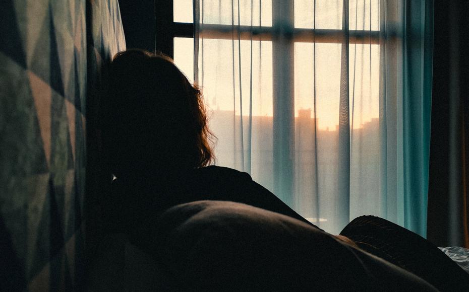 Kvinna i motljus i sovrum med gardiner för fönstret